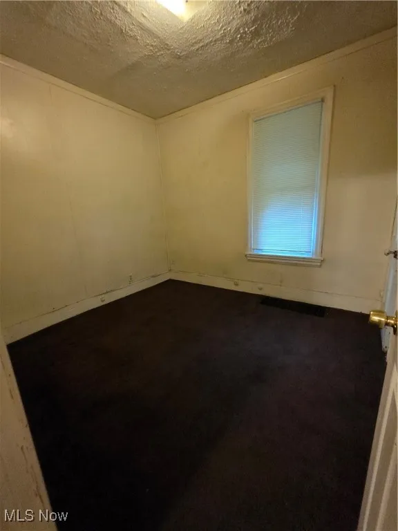 Bedroom with a textured ceiling and dark colored carpet unit 1 lower unit