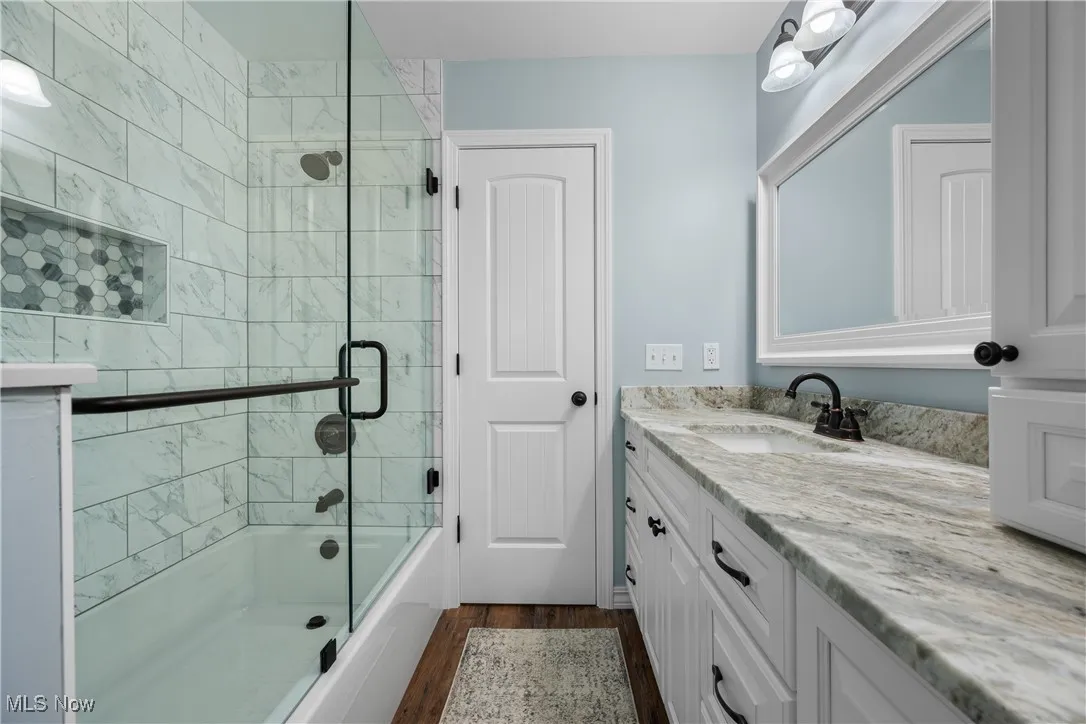 Bathroom with shower / bath combination with glass door, vanity, and dark wood-style flooring