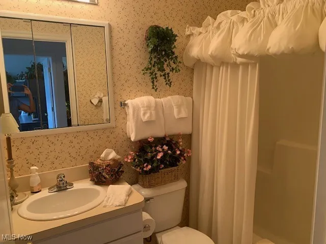 Full hall bath featuring vanity, wallpapered walls, vinyl flooring and shower / bath combination with curtain used by the 2 other bedrooms