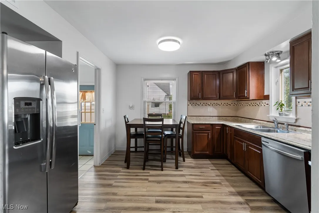 Kitchen with stainless steel appliances, light wood-type flooring, dark brown cabinets, light stone counters, and backsplash