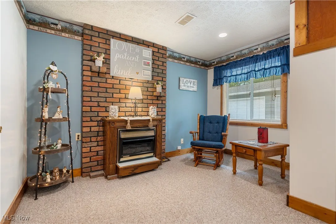 Living area featuring a fireplace, light colored carpet, and a textured ceiling