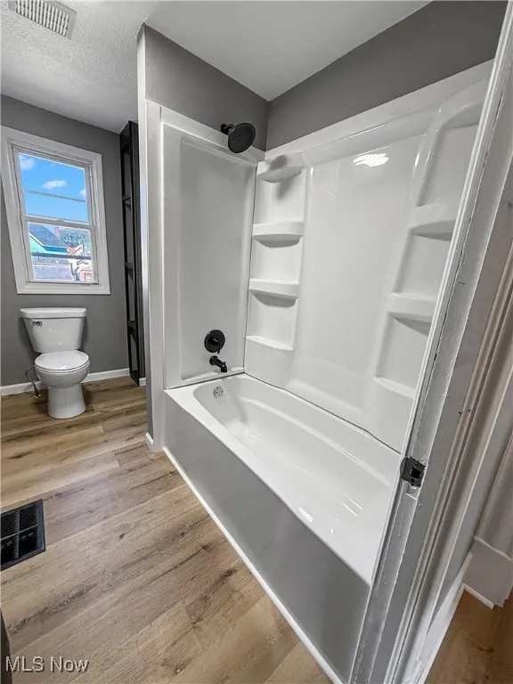 Bathroom with light wood-style floors, bathing tub / shower combination, and a textured ceiling