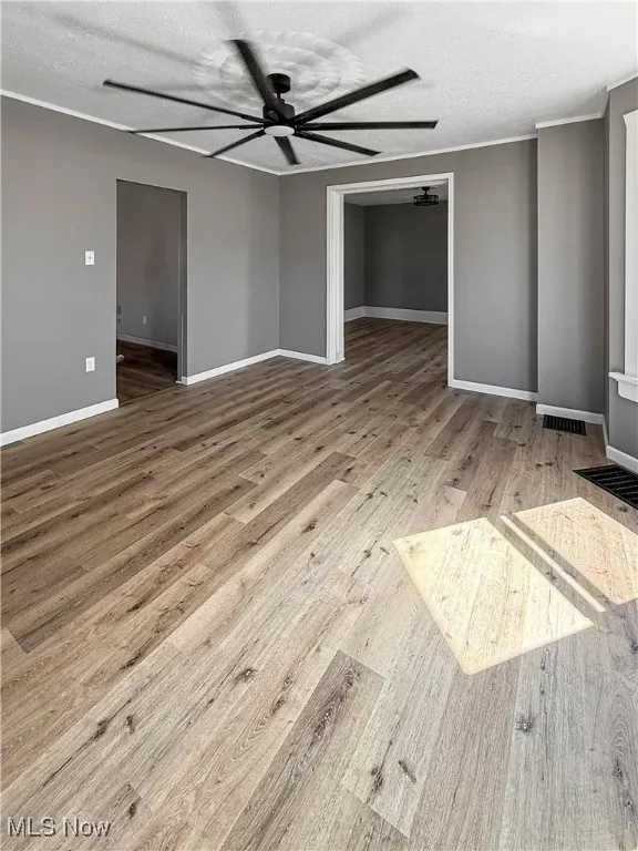 Unfurnished bedroom featuring a textured ceiling, light wood-style flooring, a spacious closet, a ceiling fan, and crown molding