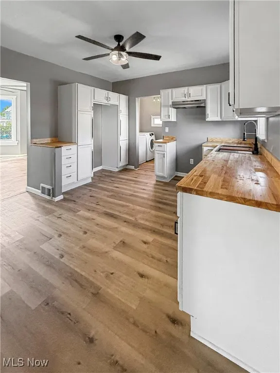 Kitchen with wooden counters, white cabinets, light wood-type flooring, and a ceiling fan