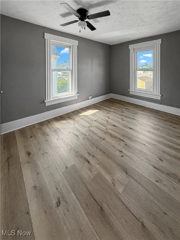 Empty room featuring a textured ceiling, light wood-type flooring, and ceiling fan