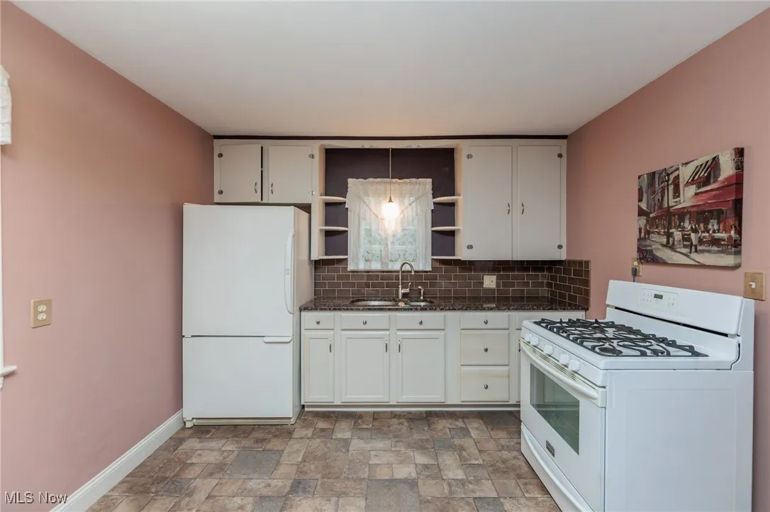 Kitchen featuring white appliances, open shelves, stone finish floors, tasteful backsplash, and hanging light fixtures