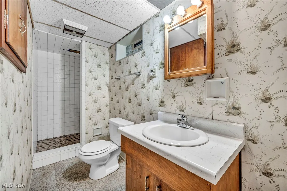 Full bathroom featuring vanity, a stall shower, and wallpapered walls