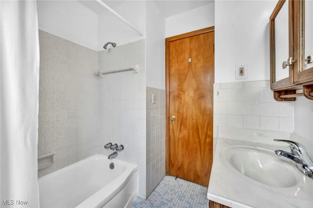 Full bath with shower / bathtub combination with curtain, tile walls, vanity, and tile patterned floors