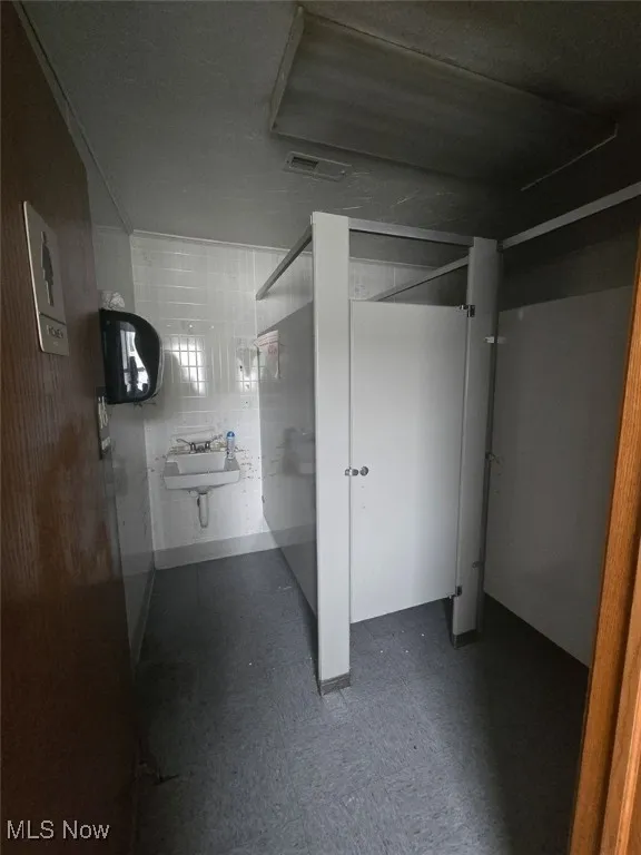 Bathroom featuring dark flooring and tile walls