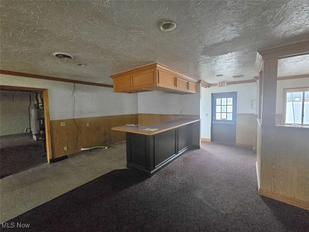 Entry with wooden walls, a wainscoted wall, ornamental molding, a peninsula, and a textured ceiling