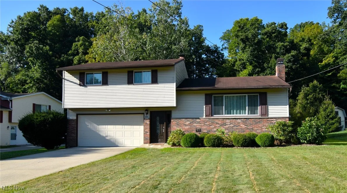 Tri-level home with brick siding, a chimney, driveway, a front yard, and an attached garage