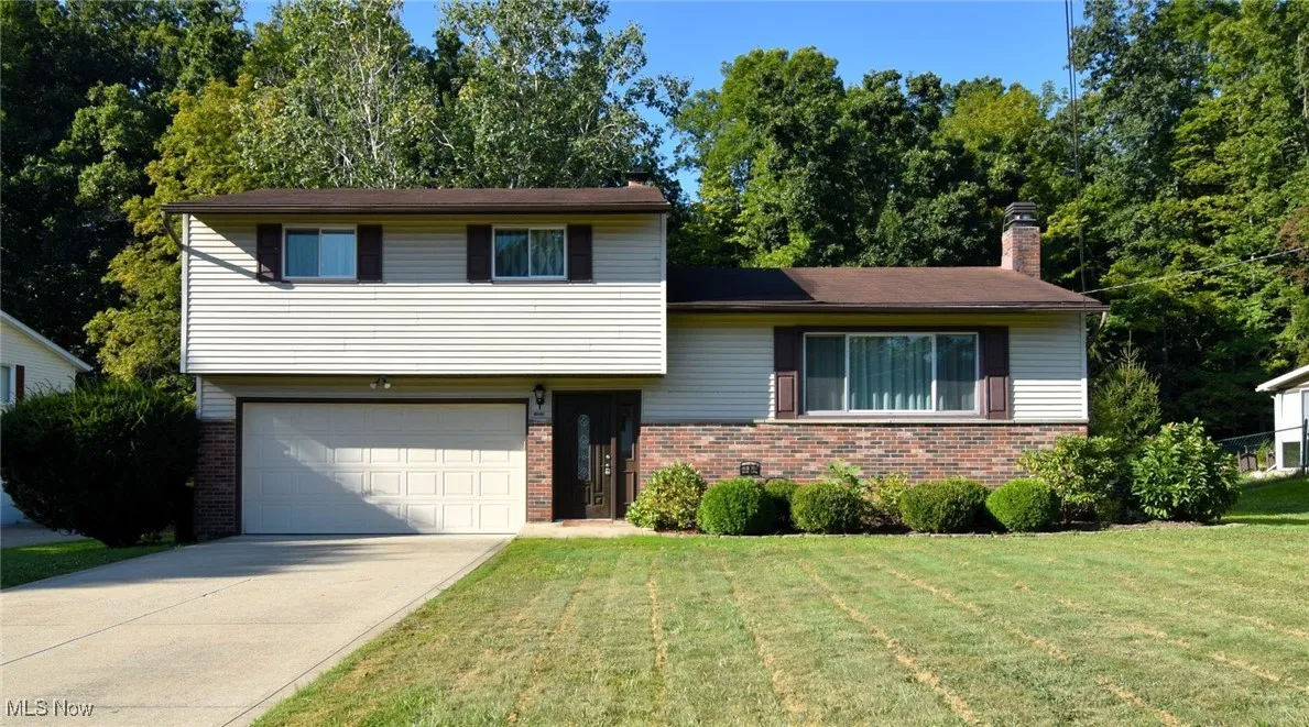 Tri-level home featuring brick siding, a chimney, driveway, an attached garage, and a front lawn