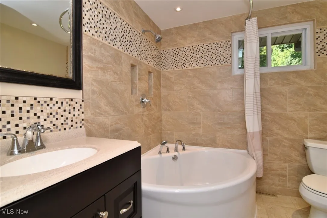 Full bathroom with tile walls, vanity, and shower / tub combo with curtain