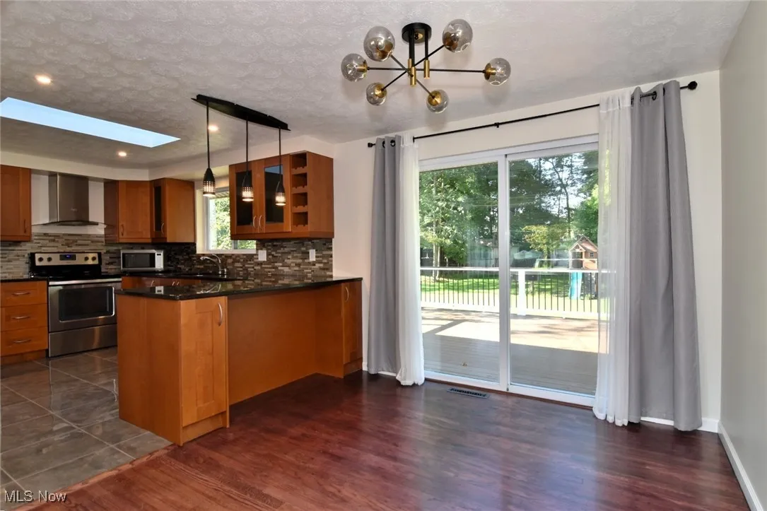 Kitchen featuring appliances with stainless steel finishes, decorative backsplash, hanging light fixtures, a textured ceiling, and brown cabinets