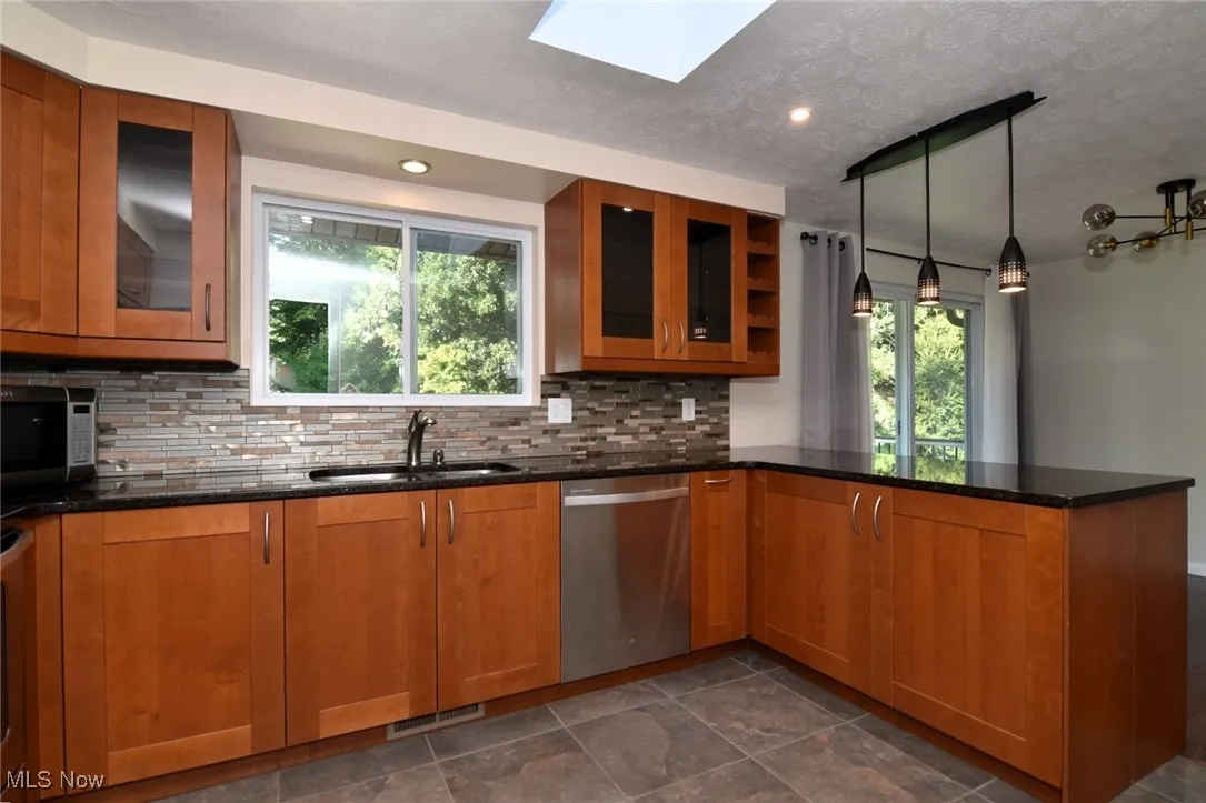 Kitchen with brown cabinets, dark stone countertops, glass insert cabinets, hanging light fixtures, and a textured ceiling