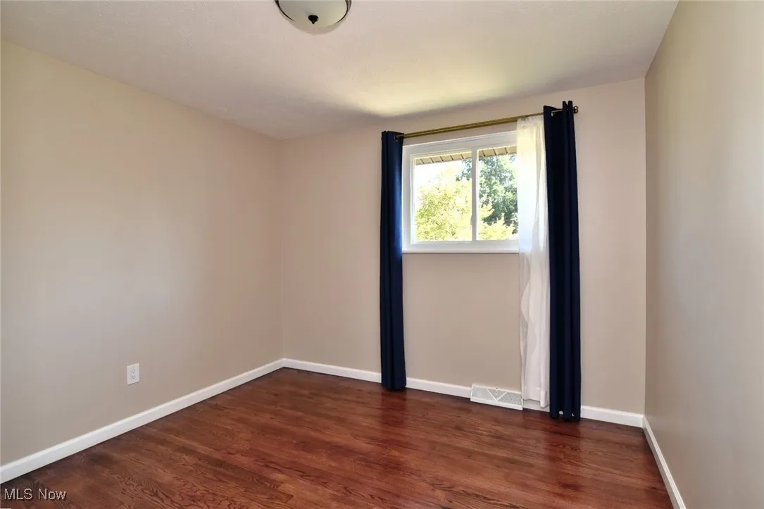 Spare room featuring dark wood-style floors and baseboards