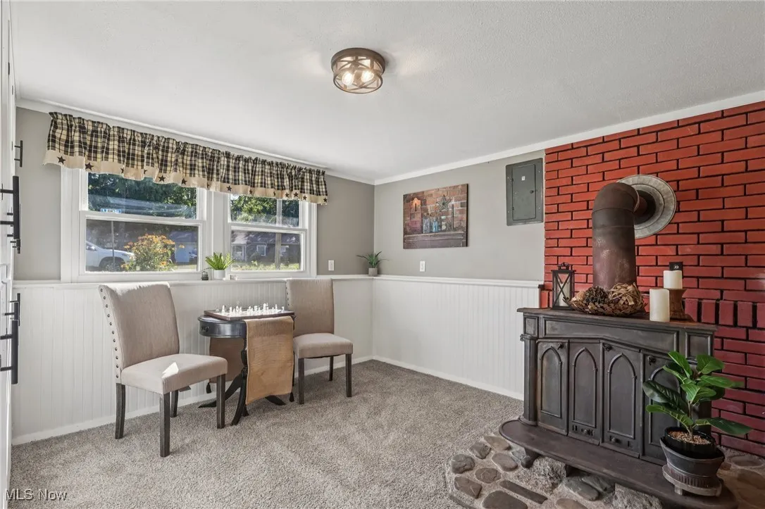 Sitting room with a wood stove, wainscoting, carpet, electric panel, and crown molding