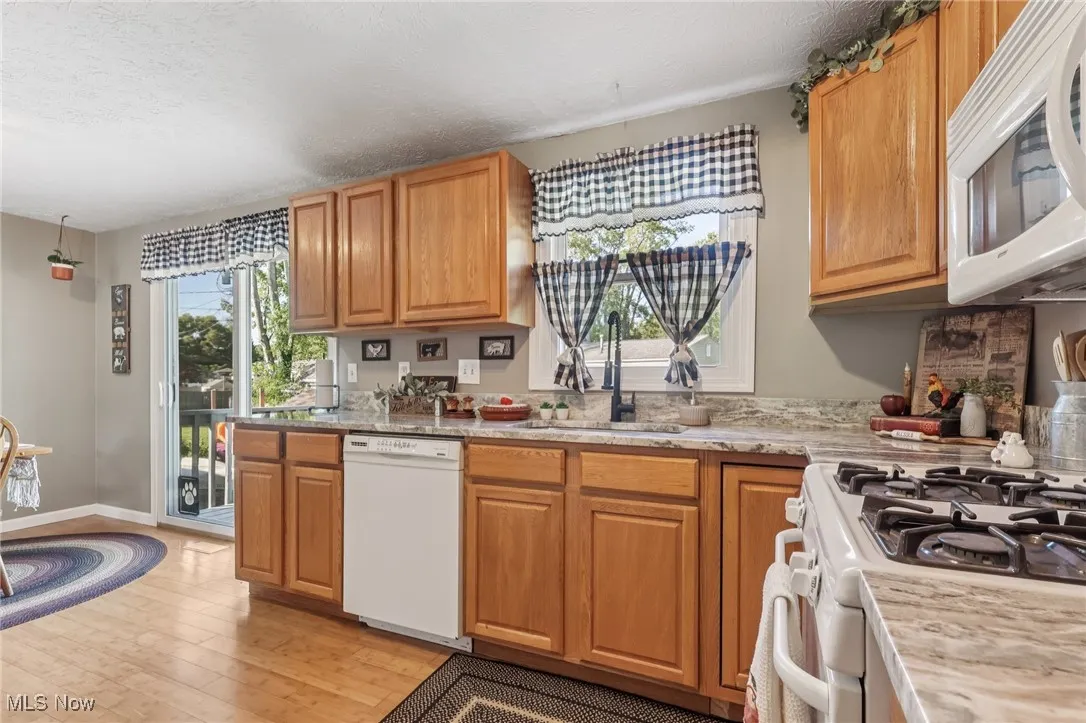 Kitchen with white appliances, brown cabinetry, light wood-type flooring, a textured ceiling, and light stone countertops