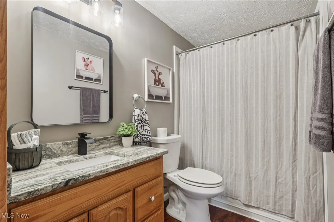 Full bath with a textured ceiling, vanity, dark wood finished floors, and shower / tub combo