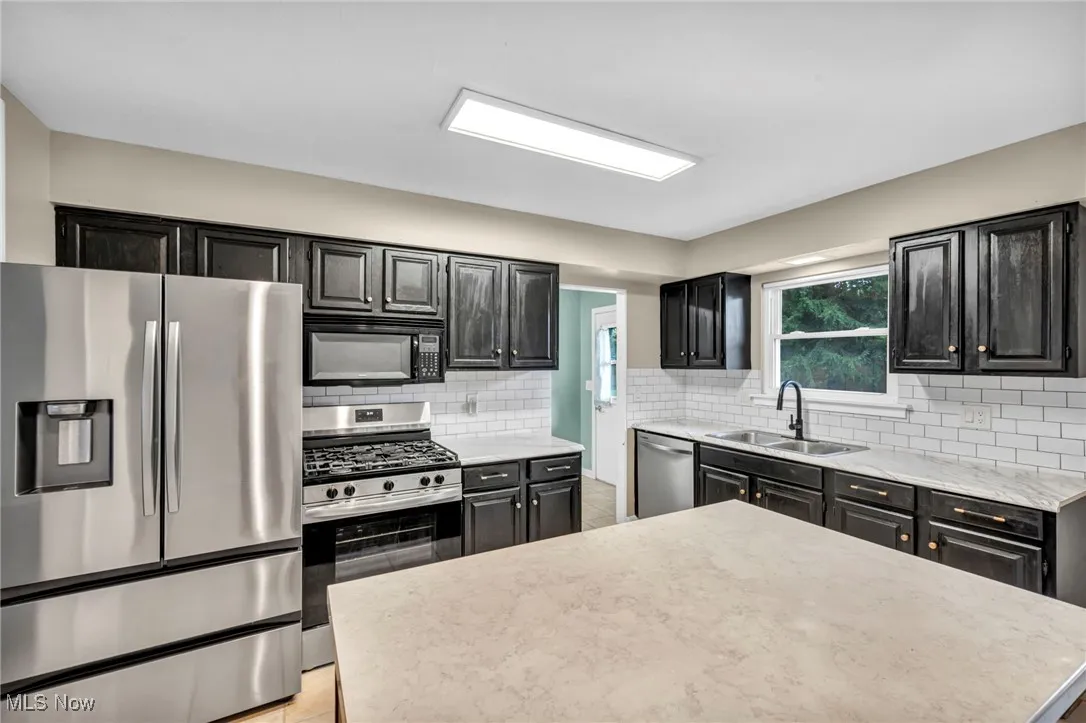 Kitchen featuring appliances with stainless steel finishes, backsplash, light tile patterned floors, and a center island