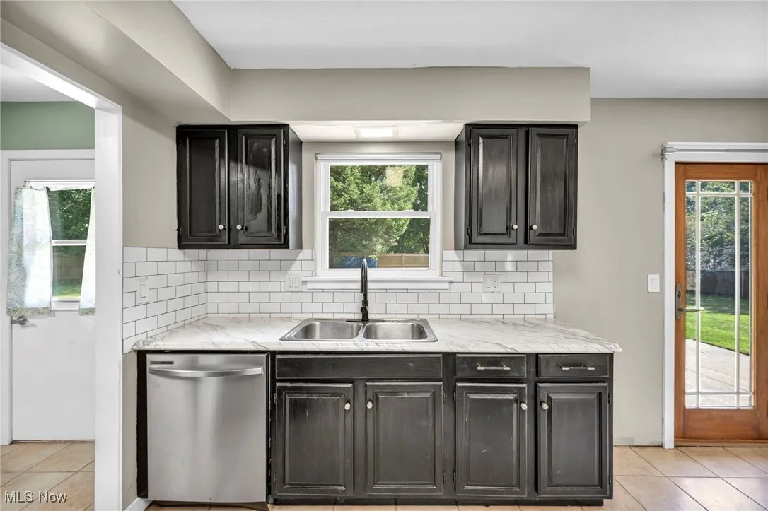 Kitchen featuring light tile patterned flooring, stainless steel dishwasher, decorative backsplash, and plenty of natural light