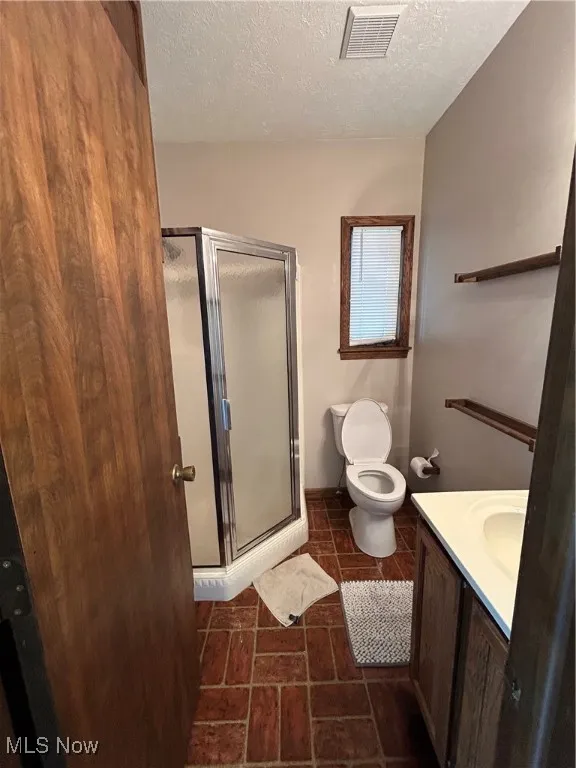 Bathroom featuring a textured ceiling, vanity, and a stall shower