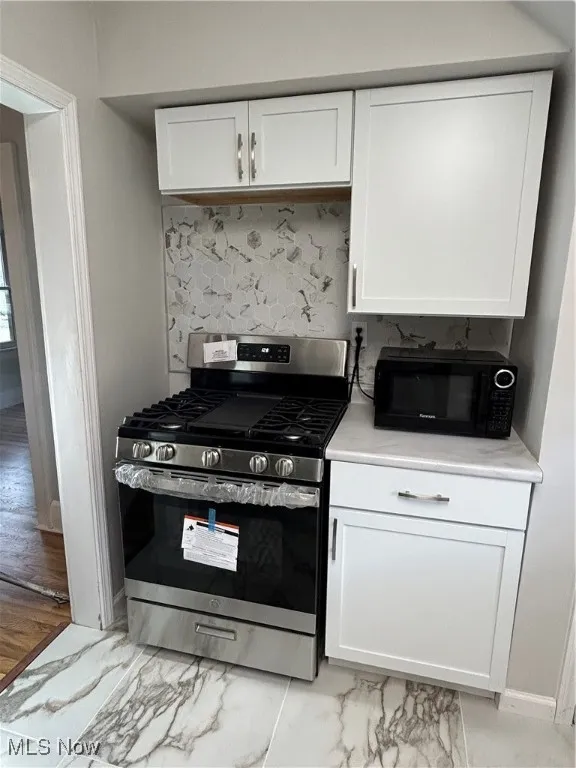 Kitchen featuring stainless steel appliances, white cabinets, tasteful backsplash, light countertops, and light marble finish flooring
