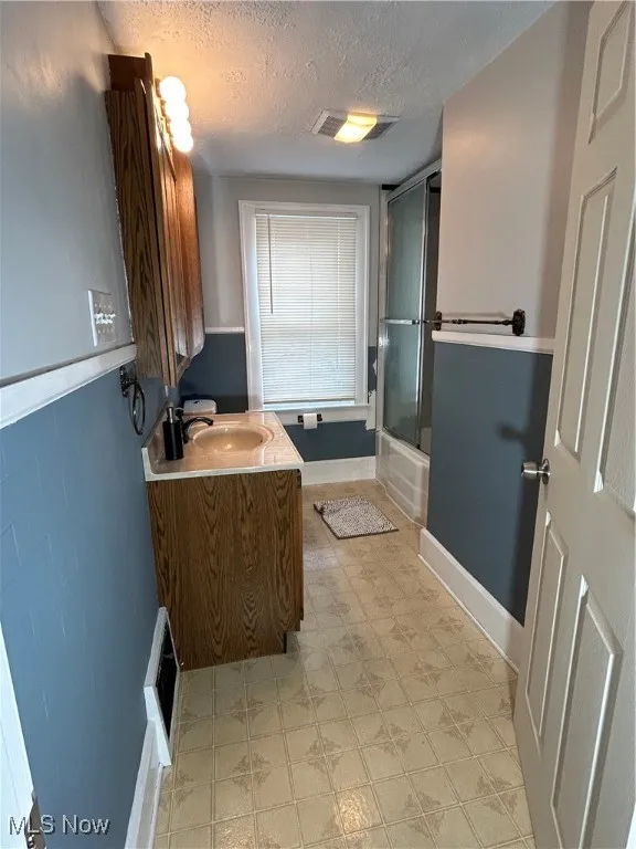 Full bathroom with vanity, a textured ceiling, and shower / bath combination with glass door