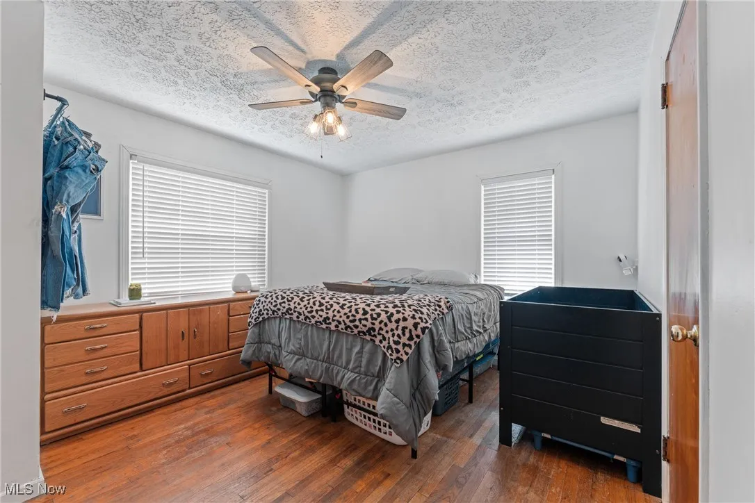 Bedroom with hardwood / wood-style floors, a ceiling fan, and a textured ceiling