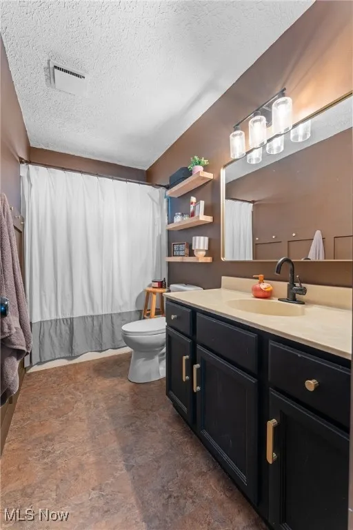 Full bath with vanity, a textured ceiling, and stone finish flooring