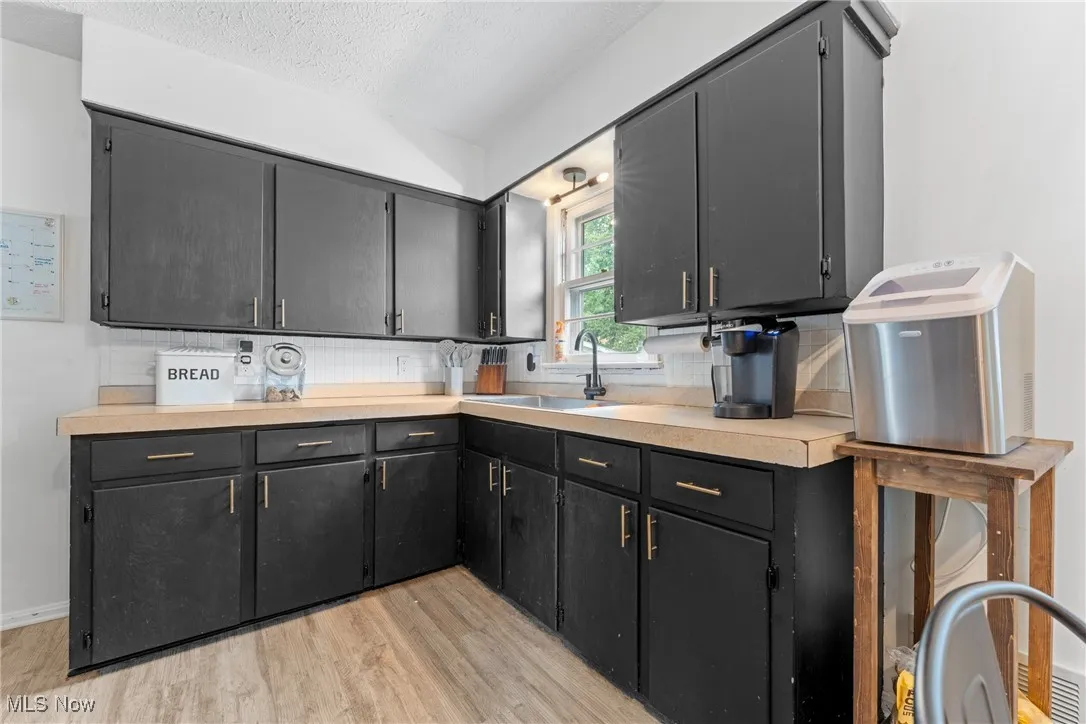 Kitchen featuring light wood-type flooring, backsplash, light countertops, a textured ceiling, and dark cabinets