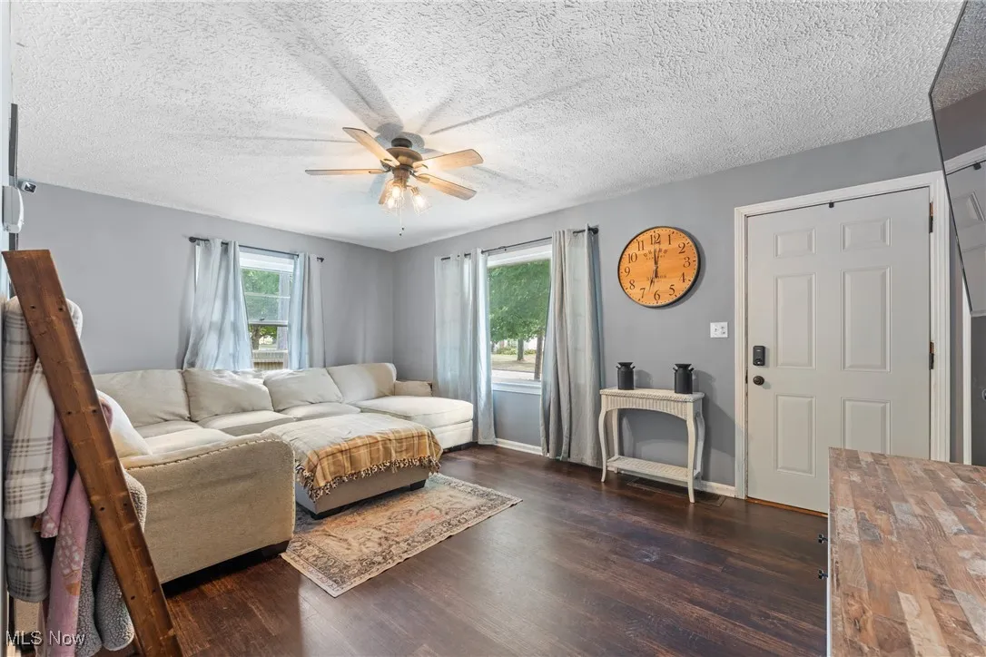 Living room with dark wood-type flooring, a textured ceiling, and ceiling fan