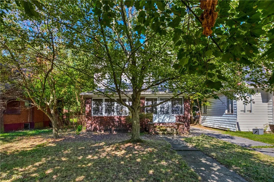 View of property hidden behind natural elements featuring brick siding and a front lawn
