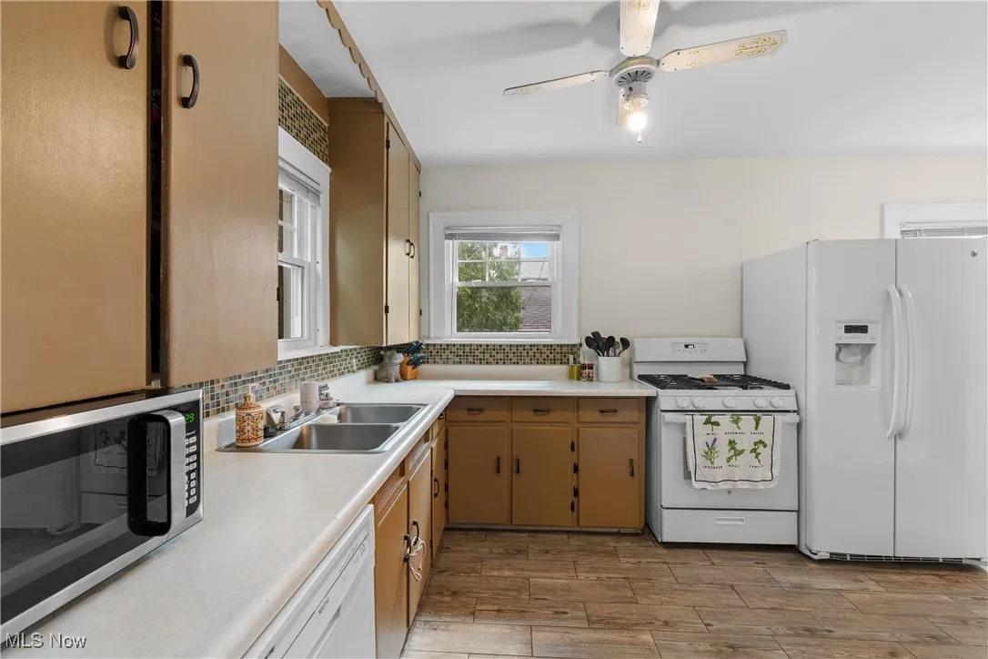 Kitchen with white appliances, light countertops, decorative backsplash, light wood finished floors, and a ceiling fan