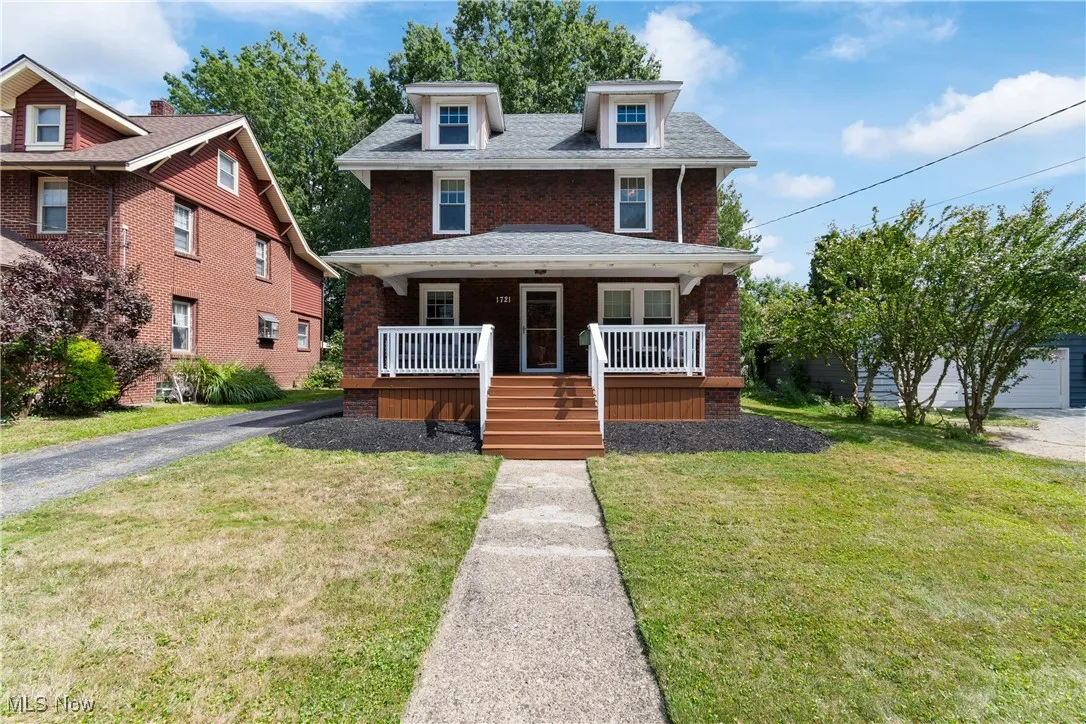 Traditional style home featuring brick siding, covered porch, a front lawn, and stairway