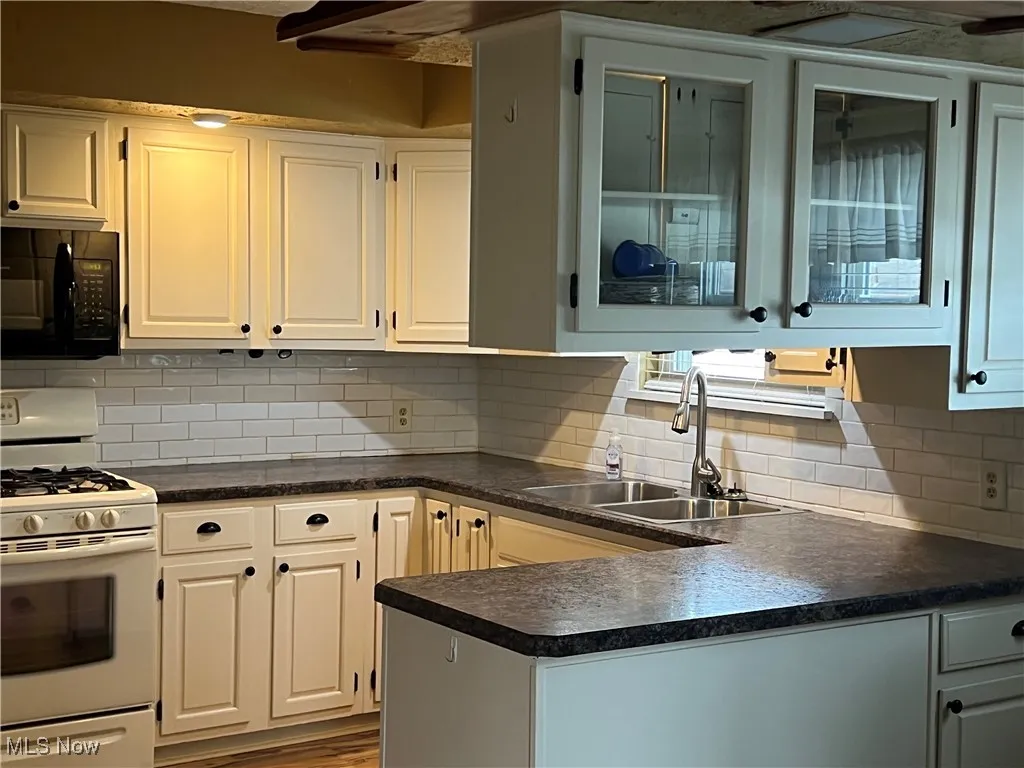 Kitchen featuring white range with gas cooktop, dark countertops, black microwave, and a peninsula