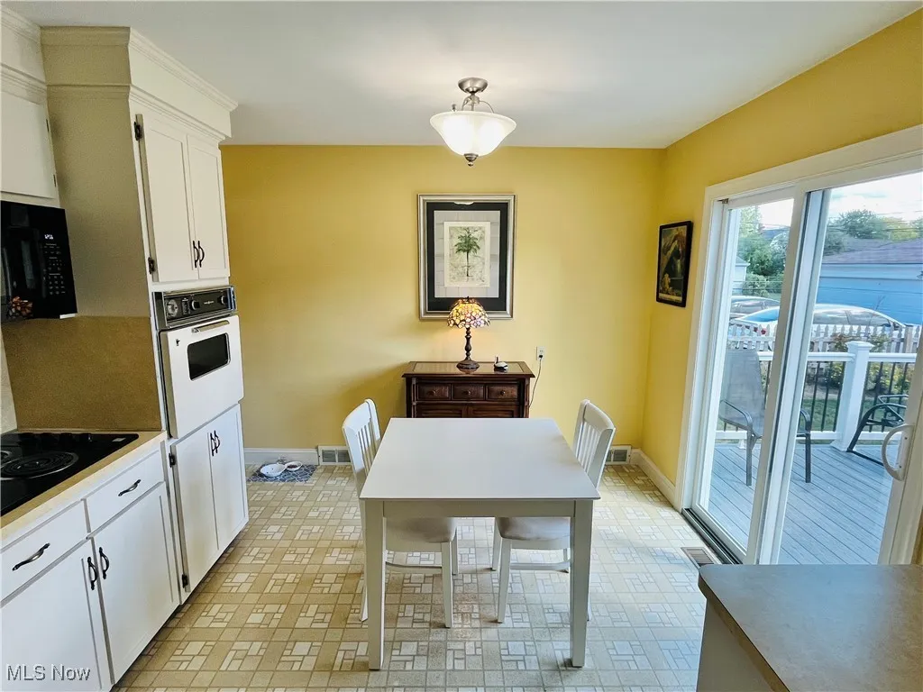 Kitchen featuring white cabinets, black appliances, light countertops, light flooring, and decorative light fixtures