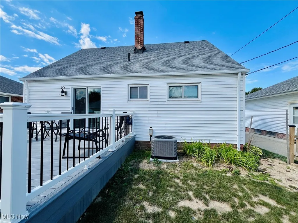 Rear view of property featuring roof with shingles, a chimney, and a wooden deck