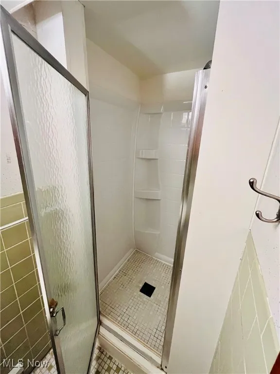 Full bath with a stall shower, tile walls, and light tile patterned flooring