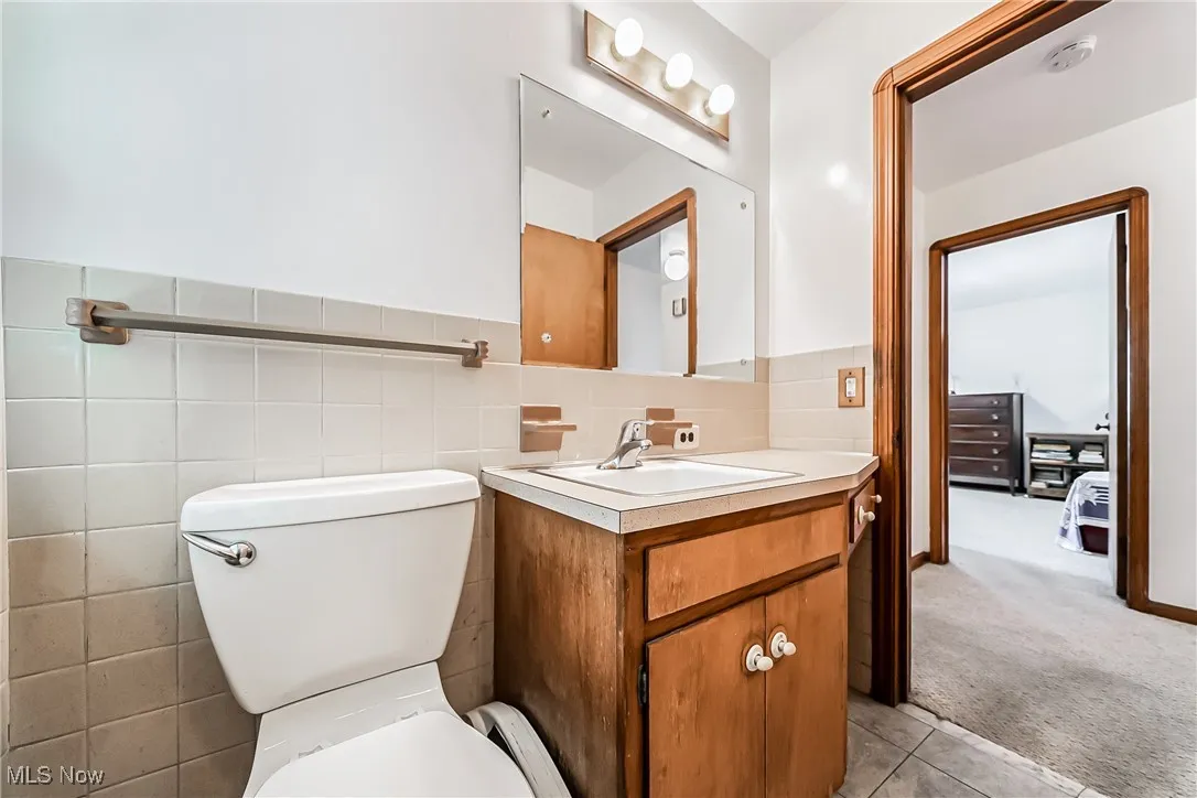 Bathroom with tile walls, tile patterned flooring, vanity, and toilet