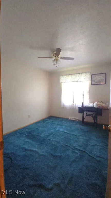 Unfurnished room featuring a textured ceiling, carpet floors, and a ceiling fan