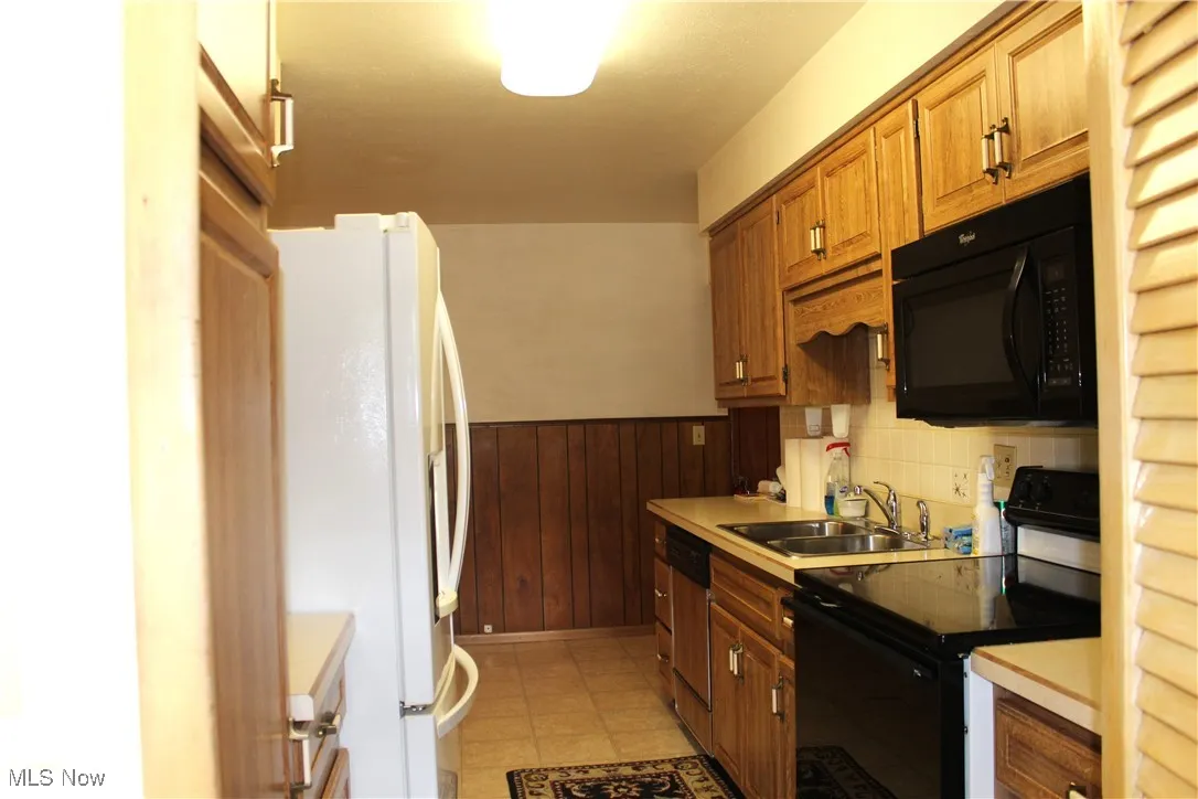 Kitchen featuring black appliances, a wainscoted wall, light countertops, wood walls, and brown cabinets