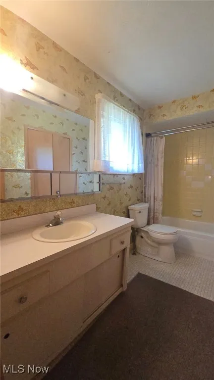 Full bath with shower / tub combo, vanity, wallpapered walls, and dark tile patterned flooring