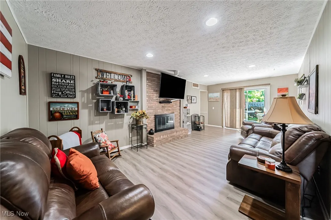 Living room with wooden walls, wood finished floors, a brick fireplace, a textured ceiling, and recessed lighting