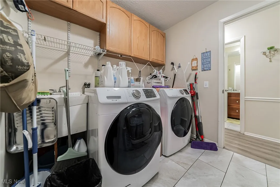 Laundry room featuring cabinet space, light tile patterned floors, a textured ceiling, and washing machine and dryer