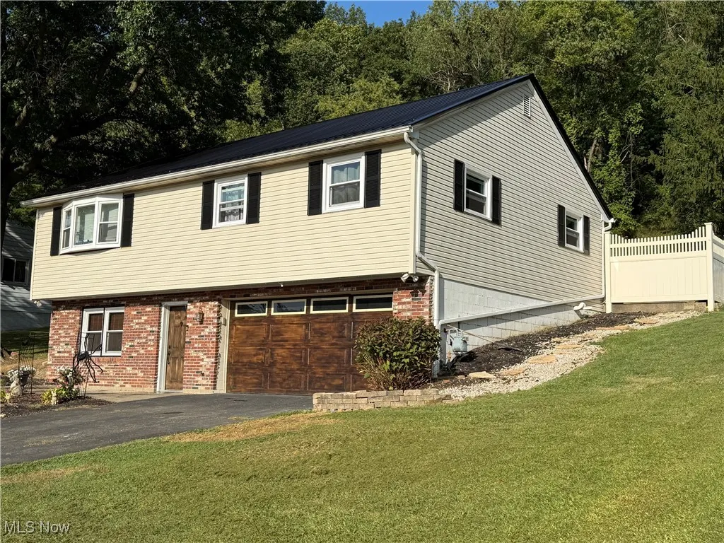 View of front facade featuring driveway, brick siding, a garage, a metal roof, and a front lawn