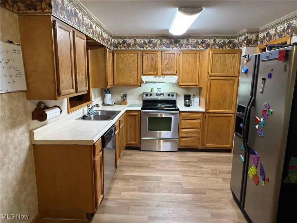 Kitchen with stainless steel appliances, brown cabinets, light countertops, and light wood-style floors