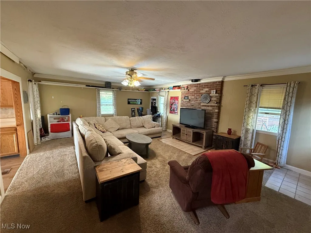 Tiled living room with a textured ceiling, carpet, ceiling fan, and ornamental molding
