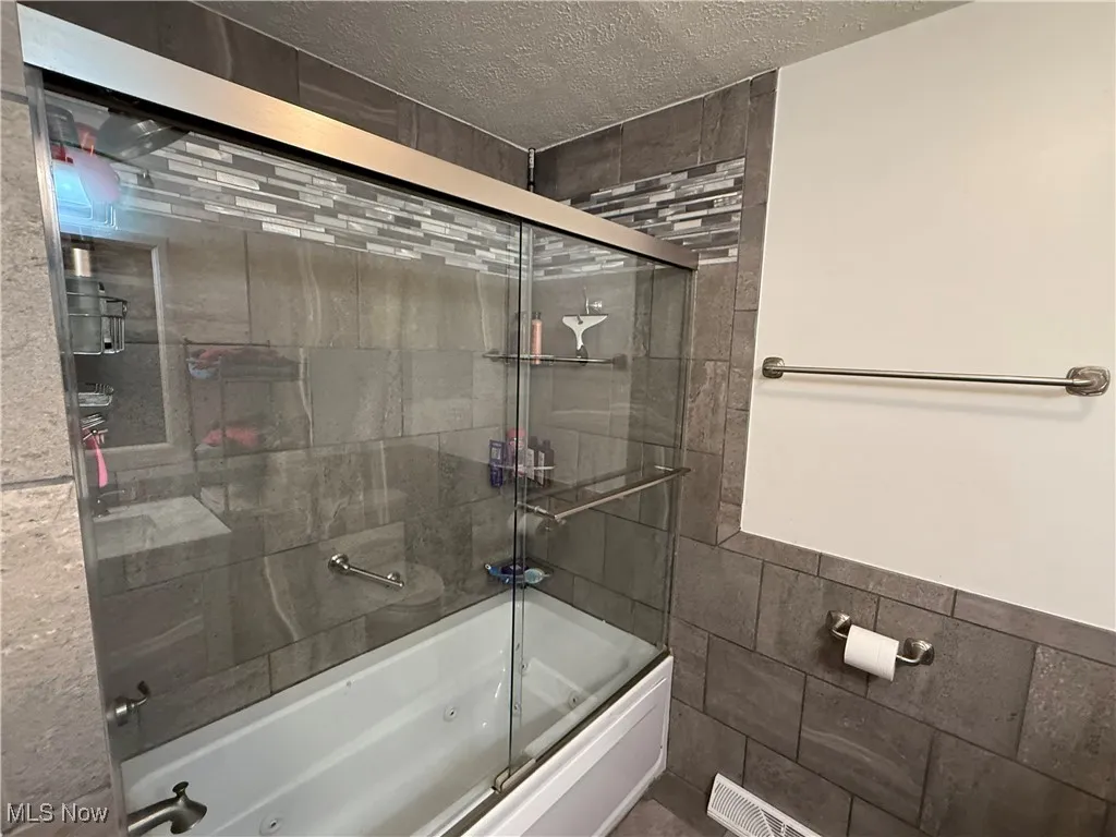 Bathroom with a combined bath / shower with jetted tub, tile walls, and a textured ceiling