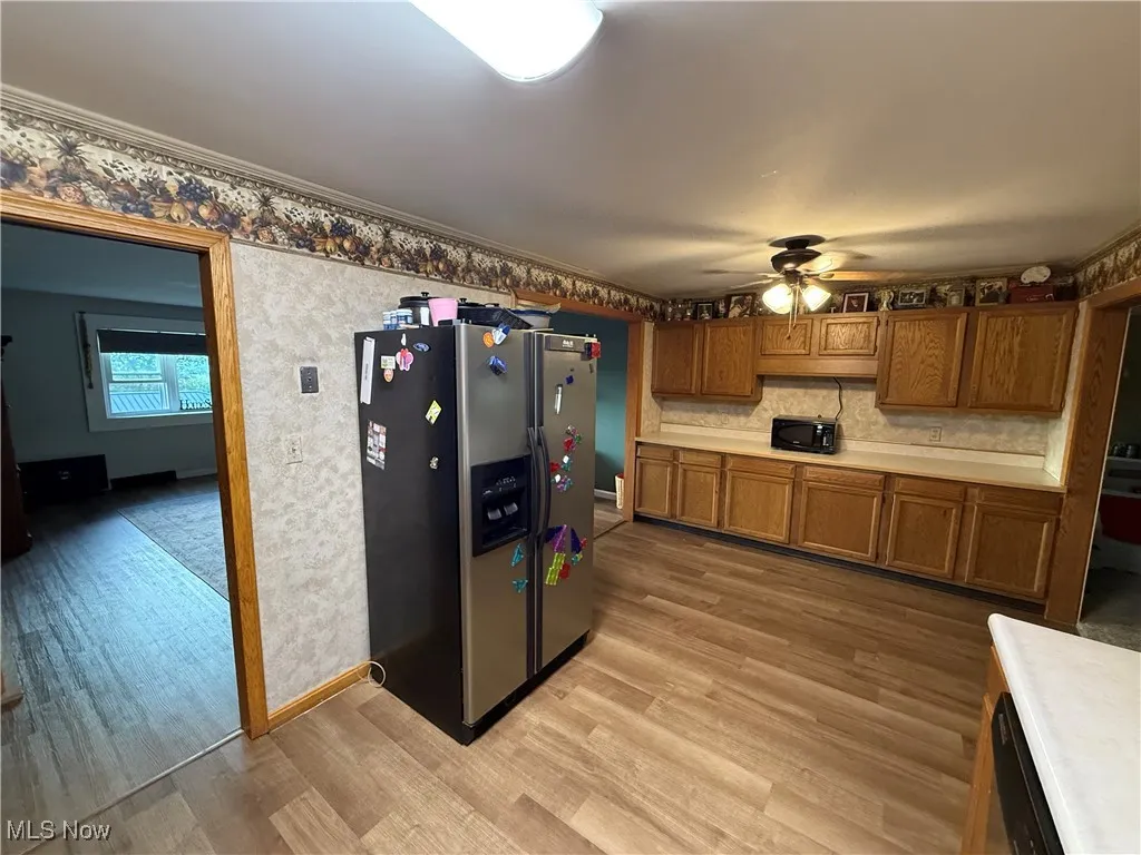 Kitchen with brown cabinetry, stainless steel refrigerator with ice dispenser, light countertops, light wood-style floors, and crown molding